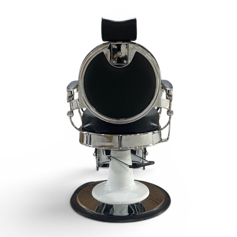 A vintage-style barber chair with a black padded seat and headrest, a round chrome mirror, and a white pedestal base with a circular black footrest, shown against a plain white background.