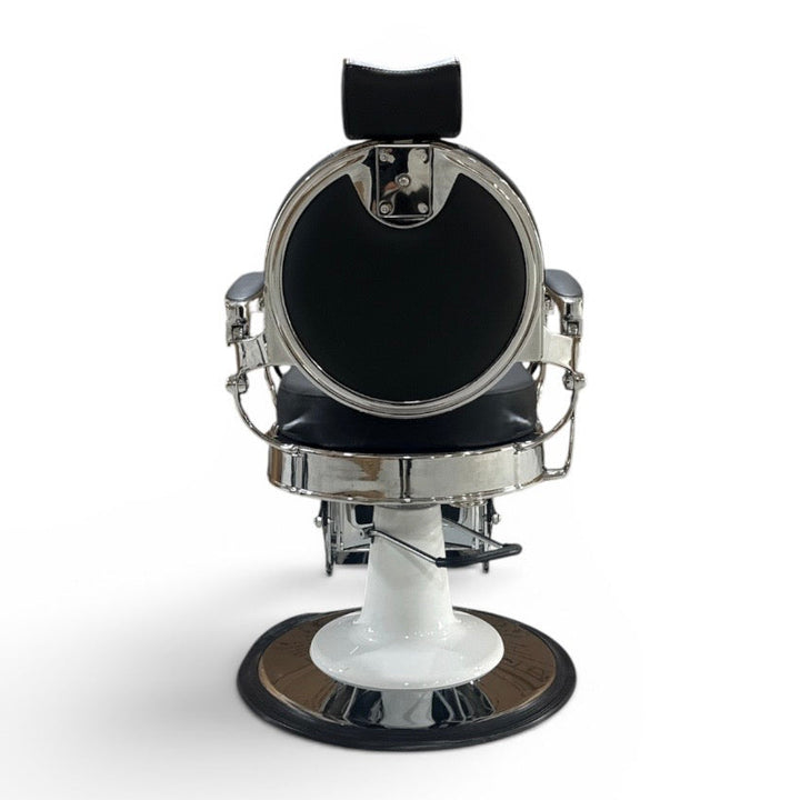 A vintage-style barber chair with a black padded seat and headrest, a round chrome mirror, and a white pedestal base with a circular black footrest, shown against a plain white background.